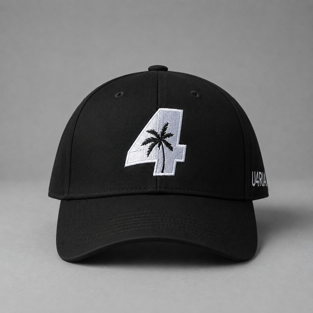 A black baseball cap with a large white embroidered number 4 on the front, featuring a black palm tree design inside the number. The side of the cap has white embroidered text reading 'U4RIA'.
